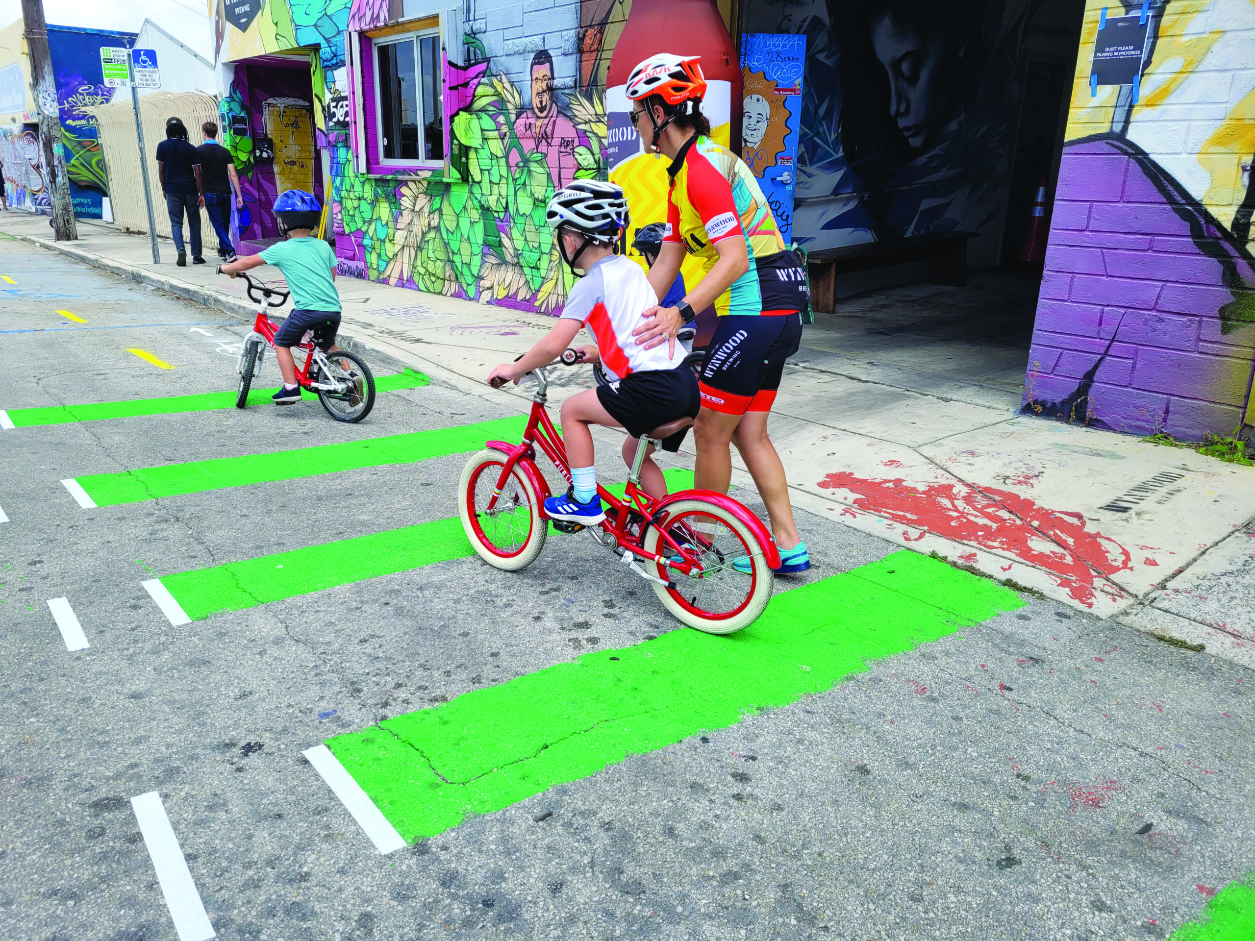 BikeSafe co-founder, Dr. Mickey Witte, assists young riders with balancing on a pop-up, low-cost demonstration bike lane created by the program. The wheelchair-accessible parking zone was recreated on the other side of the street during the event.